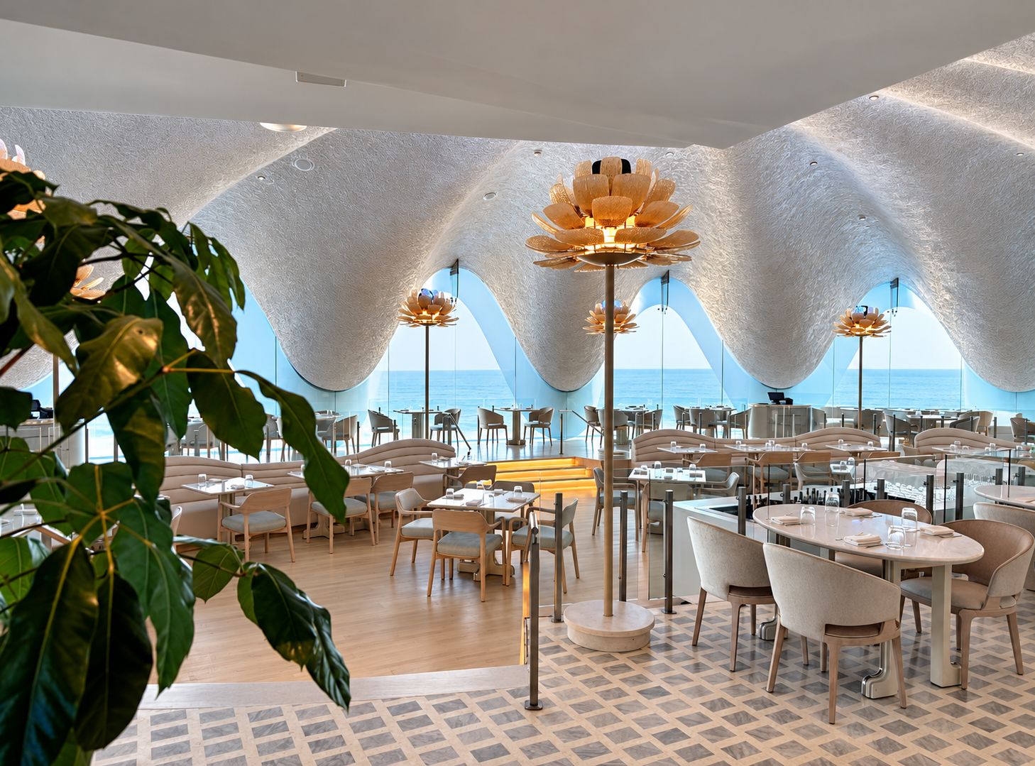 Comedor de restaurante con techo ondulado, lámparas de flor y vista al mar
